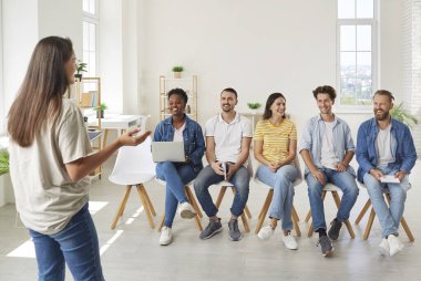 Yeni başlayanlar için gülümseyen genç meslektaşlar parlak ofisteki gündelik toplantılarda fikir alışverişinde bulunuyorlar. Enerjik kadın, önünde oturan insanlara iş hakkında fikir ve önerilerde bulunuyor.