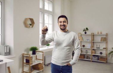 Yeni evinin anahtarlarını tutan ve kameraya gülümseyen mutlu genç adam. Heyecanlı genç bir adam gayrimenkul alıyor ve yeni bir eve taşınıyor. Emlak, mülk, taşınma ve ipotek