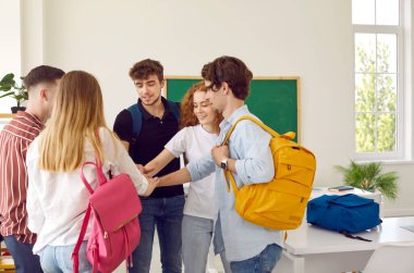 Çembere yakın duran bir grup öğrenci sınıfta ellerini birleştiriyor. Sırt çantalı gülümseyen erkekler ve kızlar gündelik giysiler giyip zaferi, birliği ve işbirliğini kutlamak için el ele tutuşuyorlar.