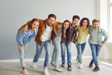 Portrait of a group of happy smiling funny friends students or colleagues in casual clothes standing together and laughing isolated on a gray background and looking positively at the camera.