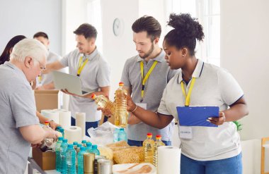 Çeşitli gönüllüler, bağış toplamak için karton kutulardaki yiyecek bağışlarını düzenliyor. Olgun ve genç insanlar yemek bankasında gönüllü olarak hayır kurumunda birlikte çalışıyorlar..