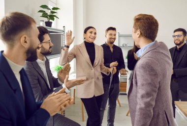 Neşeli iş arkadaşları toplantıda alkışlarken iki meslektaşı beşlik çakıyor. Kurumsal başarıyı, başarıyı, zaferi, modern ofiste başarılı anlaşmayı kutlayan meslektaşlar.