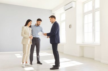 Genç ve mutlu bir çift erkek emlakçı ile anlaşmaya varıyor ve kontratı gözden geçiriyorlar. Aile ev sahibi olmaya hazır. Emlak piyasası kavramı.