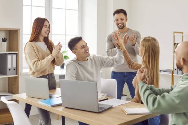 Mutlu iş ekibi başarılı bir anlaşma yapmayı kutluyor. Ofis masasında dizüstü bilgisayarla oturan mutlu, neşeli kadın ve erkek meslektaşları alkışlarken birbirlerine beşlik çakıyorlar. Takım çalışması konsepti