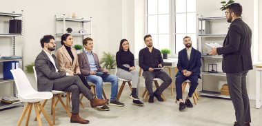 Yönetici koçu ofiste grup toplantısında konuşuyor. Erkek takım lideri eğitimde ofis çalışanlarıyla konuşuyor, çalışanlara ders veriyor, proje stratejisini tartışıyor, danışmanlık yapıyor.