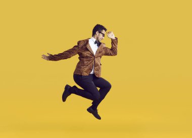 Stüdyoya atlayan neşeli siyah adam. Leopar desenli ceket, papyon ve gözlük takan neşeli etnik bir adam havada zıplıyor, parlak sarı arka planda, tüm vücudunun profilini çiziyor.