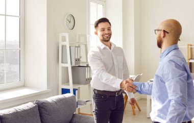 İki mutlu gülümseyen adam ofiste el sıkışıyor toplantıyı bitiriyor, başarıyı kutluyor, iş başarısını kutluyor, iyi bir anlaşma yapıyor, kontrat imzalıyor ya da yeni bir çalışanı selamlıyor..