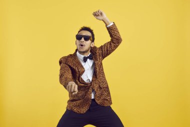 Sarı bir arka planda izole bir şekilde dans eden neşeli, pozitif, genç siyah adam. Leopar parti ceketli yakışıklı bir Afrikalı 'nın pop müzik eşliğinde dans edişinin stüdyo fotoğrafı.
