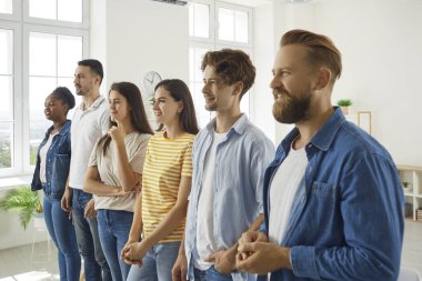 Gündelik giysiler içindeki çeşitli gençler kişisel gelişim eğitimi sırasında antrenörlerini dinliyorlar. Gülümseyen çok kültürlü erkekler ve kadınlar parlak ofiste sıraya girip dikkatle birini dinlerler..