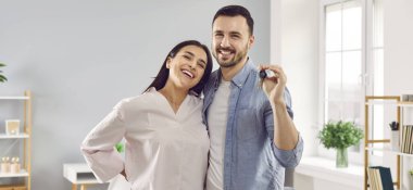 Mutlu genç çift kendi evlerinin ya da evlerinin anahtarlarını gösteriyor. Mutluluktan gülümseyen erkek ve kadınlar yeni evlerine taşınmayı kutluyorlar. Kira, gayrimenkul, taşınma konsepti