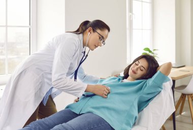 Dost canlısı jinekolog doktor klinikteki kanepede yatan hamile genç kadının kalp atışlarını inceliyor. Kadın doğum uzmanı hastasını kontrol ediyor. Bebek bekliyor..