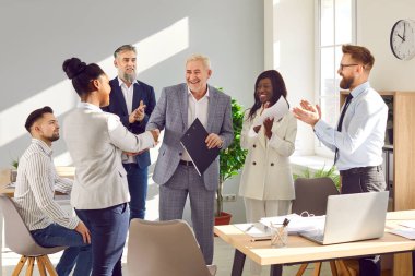 İş adamları, ofiste yapılan toplantıda işe alınan yeni elemanı alkışlıyor. Takım lideri mutlu çalışanı iyi iş çıkardığı için cesaretlendiriyor ve teşekkür ediyor.