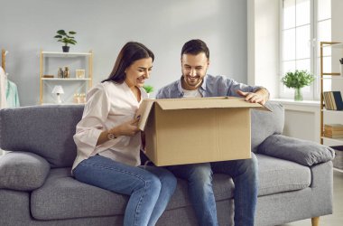 Evde karton kutuları açan heyecanlı bir aile çifti. Kadın ve erkek, oturma odasındaki kanepede otururken karton paket kutusunu açarlar. İnternetten alışveriş, internet siparişi.
