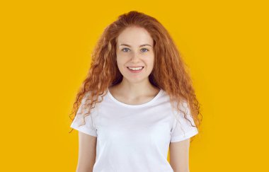 Yüzünde beyaz tişörtlü, sarı arka planda kameraya bakan uzun saçlı, kıvırcık saçlı, mutlu bir kızın portresi. İnsani samimi duygular ve görünüş kavramı.