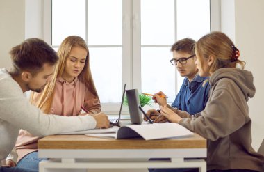 Çeşitli öğrenciler masa başı beyin fırtınası çalışmasında birlikte oturup sınava hazırlanıyorlar. Masadaki gençler ya da arkadaşlar üniversite ya da üniversite projesi için dizüstü bilgisayarda çalışıyorlar. Eğitim kavramı.