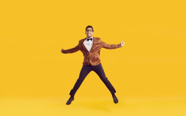 Şık giyinmiş, güzel eğlenen ve başarılarını kutlayan mutlu esmer tenli şovmen. Leopar ceketli çekici genç adam sarı arka planda izole edilmiş komik atlayışlar. Pankart. Tam uzunluk.