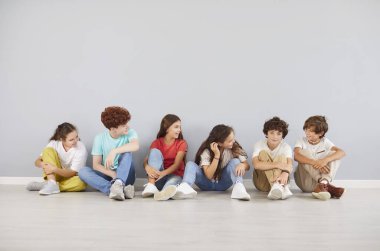 Okul çocukları, genç öğrenci arkadaşları ve sınıf arkadaşları duvarda yan yana oturan kızlar ve oğlanlar, dost canlısı eğitim ortamında gülümsüyorlar, takım iletişimini seviyorlar, günlük kıyafetlerini giyiyorlar.