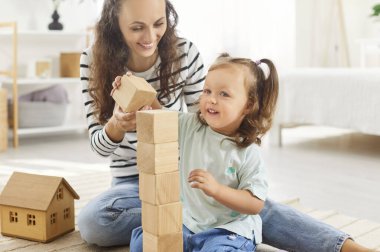 Ahşap küplerle eğitici oyunlar oynayan mutlu ve neşeli bir aile, birlikte oyuncak kulesi inşa ediyorlar. Gülümseyen anne, kızına geniş yatak odasındaki blokları dizmesinde yardım ediyor, çocuk yaratıcılığını öğreniyor..