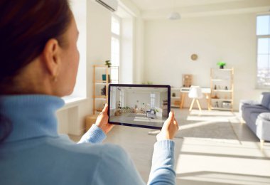 Kiralık emlakçı ya da kadın emlakçının şık bir ev dekorasyonunun akıllı tablet cihazıyla daire satmayı planlarken fotoğrafını çekmesi. Kadın ev satıcısı müşteriye video araması yapıyor.