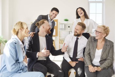 Neşeli bir grup iş arkadaşı birlikte oturup gülüyor ve sohbetten zevk alıyorlar. Mutlu gülümseyen şirket çalışanları takım oluşturma etkinliği sırasında eğleniyor. Kurumsal kültür kavramı.