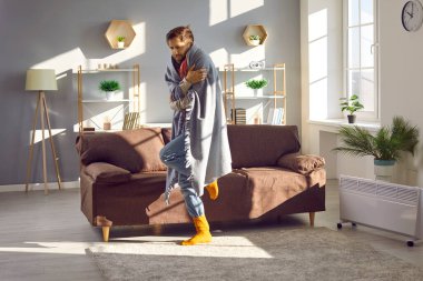 İnsan evde donar. Sıcak çorap ve battaniye giyen genç adam serin bir odada çok soğuk, sert bir kış gününde elektrikli ısıtıcıyla ısınmaya çalışıyor.