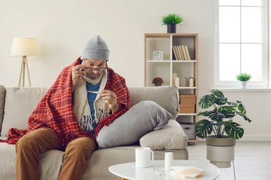 Hasta adam ateşini ölçüyor. Mevsimsel soğuk algınlığı ya da soğuk algınlığı olan bir adam evdeki kanepede oturur ve vücut ısısının aniden artması ya da düşmesi karşısında şaşkınlıkla termometreye bakar.