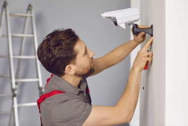Teknisyen duvara kablosuz kamera yerleştiriyor. Profesyonel işçi merdivenin üzerinde dururken tornavida kullanarak alarm sistemini kontrol ediyor. Güvenlik sistemi kavramı