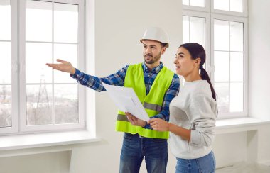 Foreman ev sahibine tasarım planını gösteriyor. Ev ve iç dekorasyonun bina içinde genç bir kadınla yenileme planlarını tartışan kasklı bir işçi. Ev tasarımını gösteren işçiler