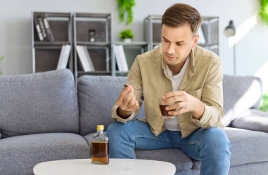 Alkol bağımlısı bir adam evde sigara ve içki içiyor. Sigara bağımlılığı, istismar, depresyon ve sağlık sorunu olan bir bardak ve viski şişesi. Alkolizm sağlığa ve hayata zarar verir.