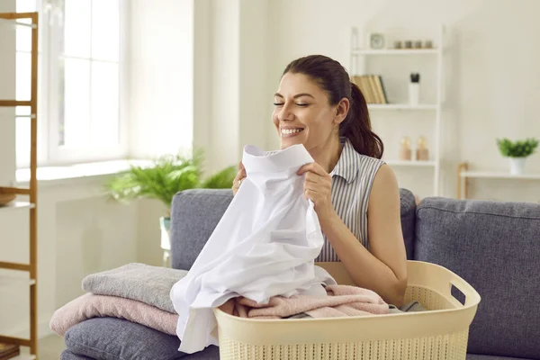 Kadın temiz çamaşır kokuyor. Kanepede çamaşır sepetiyle oturan, temiz, yıkanmış, beyaz gömlekli, taze kokan, doğal aromalı ve gülümseyen mutlu bir ev hanımı.