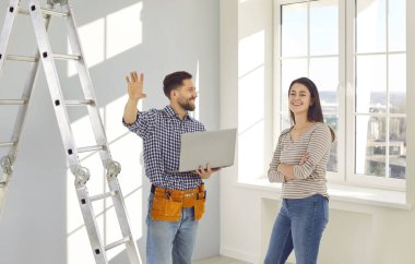 Genç evli çift taşınma gününden sonra boş bir odada bir apartman tadilatı ve tasarım projesi planlıyor. Gülümseyen mutlu adam ve kadın dizüstü bilgisayarla yeni evlerinin onarımını tartışıyorlar.