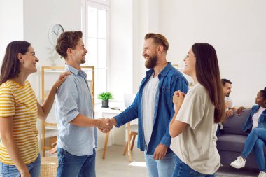 Görüşme sırasında gülümseyen ve tokalaşan mutlu arkadaşlar. Gülümseyen adam, arkadaşça bir toplantıda bir başkasıyla tanışıyor, kızlar onları tanıştırıyor. Mutlu insanlar birlikte takılırken tanışırlar.