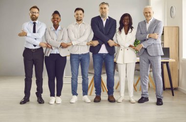 Bir grup iş adamı sıraya girip kameraya bakıyor, el ele tutuşuyor ve ofiste gülümsüyor. Şirket çalışanlarının ya da bir grup çalışanın portresi. Takım çalışması konsepti.