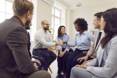 Afrikalı Amerikalı bir kadın başarıyı kutlayan bir adamla el sıkışıyor, anlaşma yapıyor, iş başarısı sağlıyor ya da bir grup insanla iş yerinde bir araya gelip toplantı yapıyor..