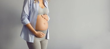 Bebek bekleyen genç bir anne. Tanımlanamayan hamile bir kadın stüdyoda duruyor ve kocaman, çıplak karnını okşuyor. Gri metin telif alanı afişi başlık arkaplanı. Kesilmiş atış. Hamilelik konsepti