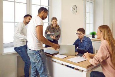 Çok ırklı öğrenciler çalışma toplantısında okul projesini birlikte çalışırlar ve hazırlarlar. Modern cihazların önünde oturan kızlar ve oğlanlar iletişim kurar ve not defterlerine notlar yazarlar. Eğitim kavramı.