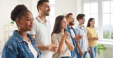 İş seminerinde farklı dinleyiciler konuşma dinliyor. Bir grup mutlu karışık ırk tişörtlü ve kot pantolonlu insanlar ofiste sıraya girmiş, başka tarafa bakıyor ve iş konuşmacılarını dinliyorlar.