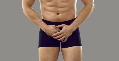 İç çamaşırlı bir adam gri arka planda dikilip acı dolu kasık bölgesini kapatıyor. Kesilmiş atış, afiş. Erkek mahrem sağlık sorunları, cinsel yolla bulaşan hastalıklar, testis kanseri kavramı