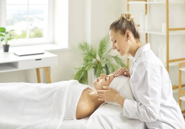 Genç bayan kozmetik uzmanı ya da cilt bakımını güzellik salonunda ya da sağlık kliniğinde gülümseyen bir kız müşteriye yaptırıyor. Yüz masajı, cilt bakımı ve kozmetik konsepti.