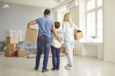 Baba, anne ve oğul yeni bir evde ya da dairede, taşınan kutularla birlikte dururlar ve aile taşınması işaretlenir. Beraberlik, sahiplik ve yeni bir hayatın heyecanı..