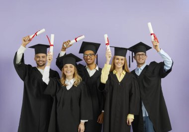 Tebrikler, mezun. Mutlu, neşeli, çeşitli uluslararası üniversite öğrencileri mezuniyet töreninde kırmızı kurdeleli kağıt diplomalar yükseltiyorlar.