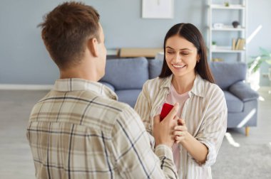 Elinde kırmızı hediye kutusu olan genç adam mutlu bir kız arkadaşa evlenme teklif ediyor. Adamın biri evinde oturan neşeli kız arkadaşına nişan yüzüğü ya da mücevherle sürpriz bir hediye veriyor..