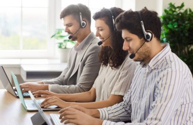 Kulaklık takan çağrı merkezi ajanları ofis masasında dizüstü bilgisayarlarla çalışıyorlar. Tele-pazarlama operatörleri müşterileri destekliyor, müşterilere yardım etmek için acil aramalar, sohbetler ve e-postalarla çalışan gülümseyen yardım masası ekibi