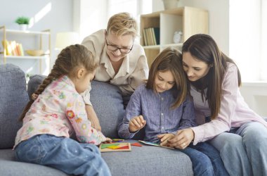 Modern oturma odasındaki kanepede oturan mutlu aile yetişkinler ve iki çocuk oyun oynuyorlar. Oyun oynuyorlar ve oyun oynuyorlar. Oyun ile etkileşime geçiyorlar.