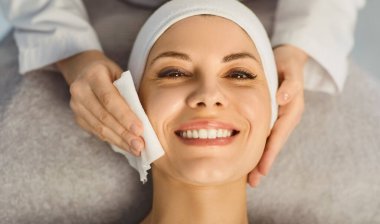 Güzellik salonunda yüz bakımı yaptırırken ve güzellik kliniğindeki güzellik uzmanından güzellik tedavisi görürken kameraya gülümseyen güzel bir kadın müşterinin portresi..