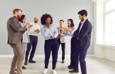 Afrikalı Amerikalı kadın ofis toplantısında iş arkadaşlarıyla dans ediyor, başarıyı kutluyor. İnsanlar neşeli ve hayat dolu. İş dünyasındaki birlik ve başarıyı yansıtıyor..