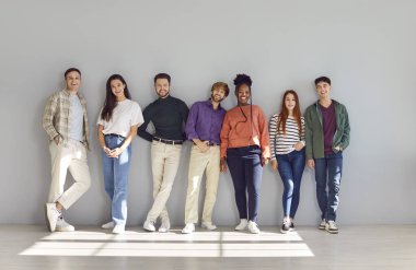 Duvarın yanında kameraya bakarken gülümseyen gençlerin toplu portresi. Çeşitli mutlu çok ırklı ve çok uluslu öğrenciler parlak bir stüdyoda poz veriyorlar..