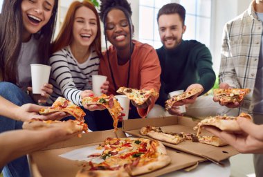 Çeşitli neşeli arkadaşlar evde parti sırasında lezzetli pizzalar yiyorlar. Tasasız, mutlu, çok ırklı genç erkek ve kadınlar lezzetli pizzaların tadını çıkarıyorlar. Ev partisi konsepti.
