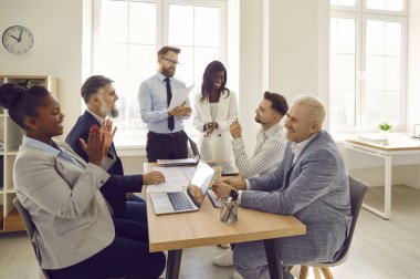 Çeşitli iş adamları iş toplantısı sırasında eğleniyor. Bir grup mutlu genç ve yaşlı çoklu etnik gruptan insan bir ofis masasında oturup komik bir şeye gülüyorlar.