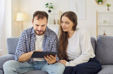 Evlerinde internet gezinen tabletli bir çift. Kanepede birlikte oturuyorlar, birlikte arıyorlar, seçenekleri karşılaştırıyorlar, ve rahat oturma odasındaki uygulamadan satın alma planları yapıyorlar. Çevrim içi alışveriş ve teknoloji.